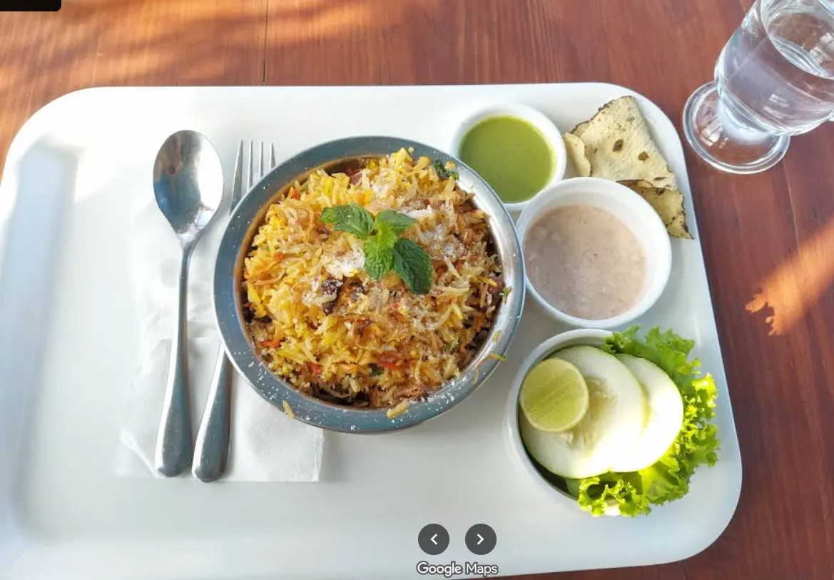 A bowl of fragrant biryani served with raita, papad and lemon