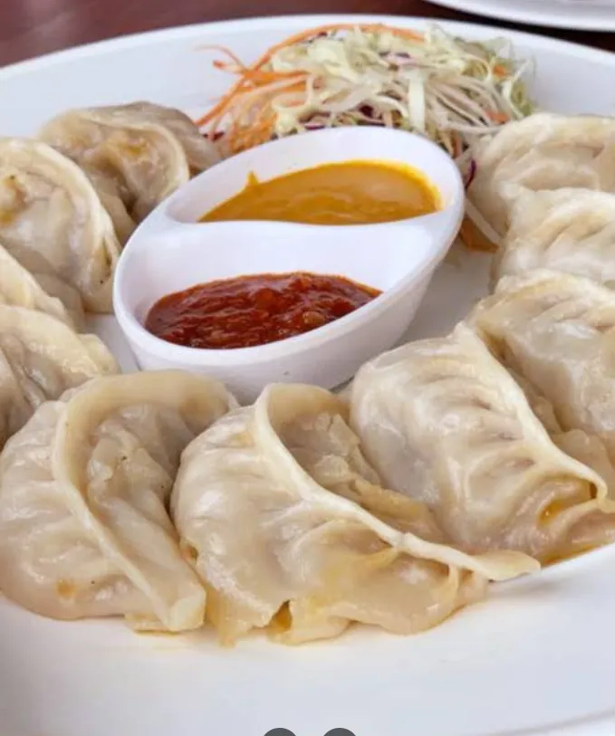 A plate of steamed Nepalese momos with tomato achar and fresh salad